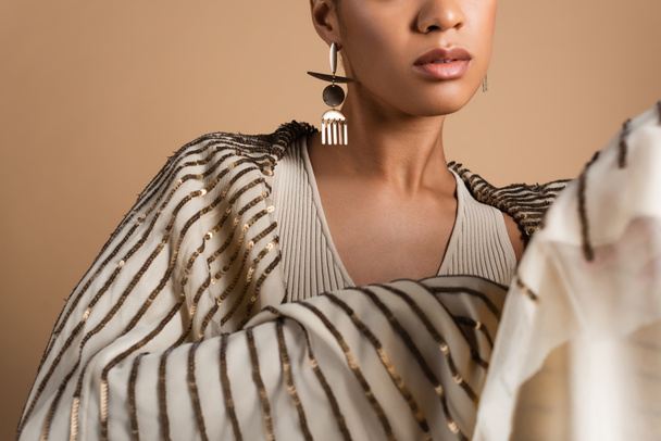 cropped view of rich african american woman in golden jewelry posing with shawl isolated on beige  - 写真・画像