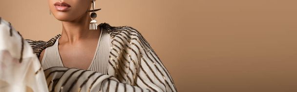 обрезанный вид на богатую африканскую американку в золотых украшениях позирует изолированы на бежевый, баннер - Фото, изображение