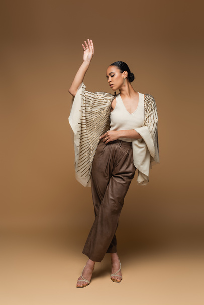 full length of african american woman in golden jewelry and shawl posing on beige  - Photo, Image