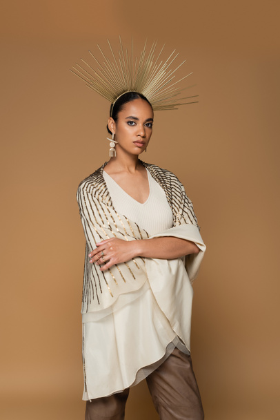 brunette african american woman in shiny shawl and golden crown posing with crossed arms isolated on beige  - Foto, Bild