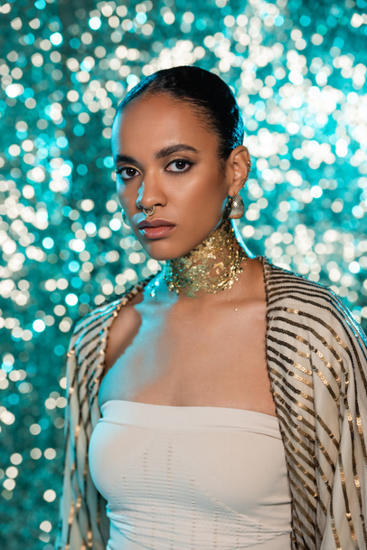 african american woman with piercing and gold on neck posing in shawl on shiny blue background  - Φωτογραφία, εικόνα