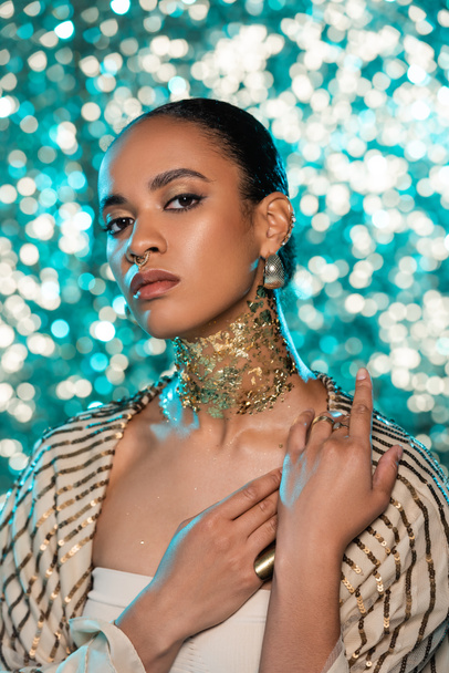 african american woman with piercing and gold on neck posing on sparkling blue background  - Foto, Imagem
