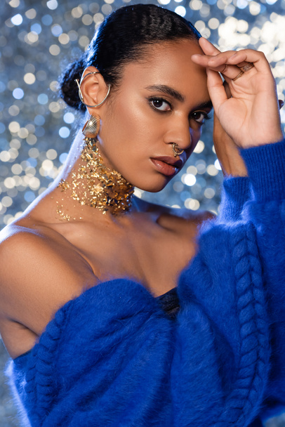 Portrait of fashionable african american woman with golden accessories looking at camera on sparkling background  - Photo, Image