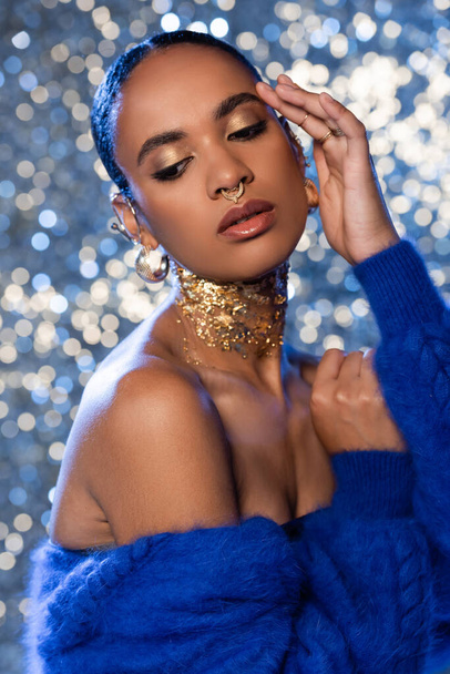 Trendy african american model with golden accessories and blue faux fur jacket on sparkling background  - Fotó, kép