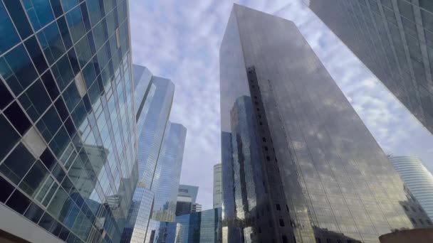 De glazen wolkenkrabbers reflecteren de blauwe lucht met wolken. Camera beweging in een moderne zakenwijk. Succesvol zakelijk concept. Hoge kwaliteit 4k beeldmateriaal - Video