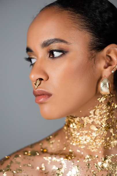Portrait of young african american model with golden foil on neck looking away isolated on grey  - Photo, Image
