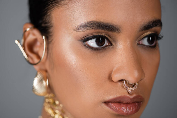 close-up uitzicht op afrikaanse amerikaanse vrouw met gouden piercing weg te kijken geïsoleerd op grijs  - Foto, afbeelding