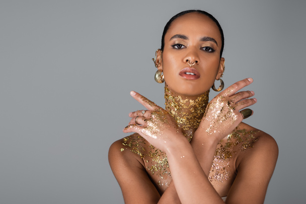 Trendy african american model with golden foil on body looking at camera isolated on grey  - Fotografie, Obrázek