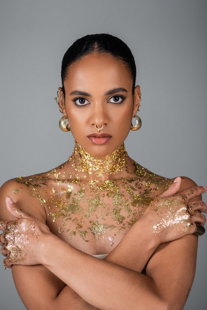 Portrait of african american woman with golden foil on body and hands looking at camera isolated on grey  - Fotografie, Obrázek