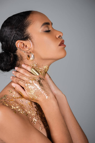 Side view of stylish african american woman with golden foil on hands touching neck isolated on grey  - Foto, Imagem
