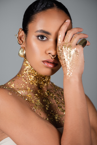 Young african american model with foil on hand and chest covering face isolated on grey  - Photo, Image