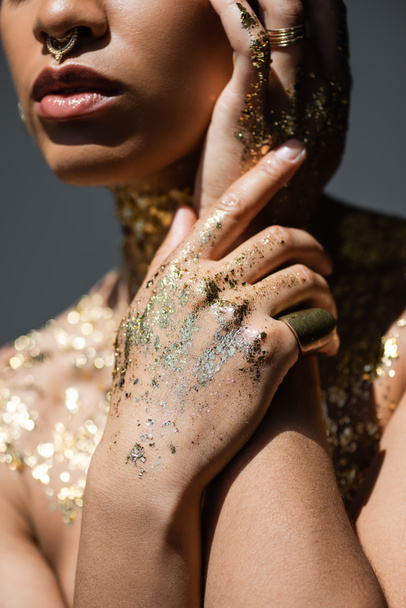 Καλλιεργημένη άποψη του μοντέρνου αφρικανικού αμερικανικού μοντέλου με το χρυσό φύλλο στα χέρια και το σώμα απομονώνονται σε γκρι με το φως  - Φωτογραφία, εικόνα