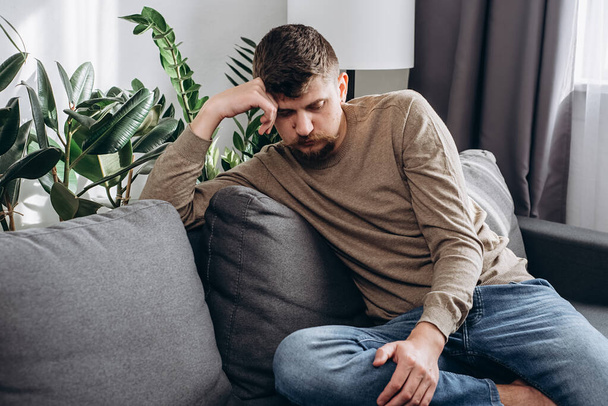 Thoughtful male pondering over issue or trouble. Unhappy caucasian man sitting on sofa thinking about problem solution, focused young guy lost on thoughts making decision on considering something - Fotó, kép