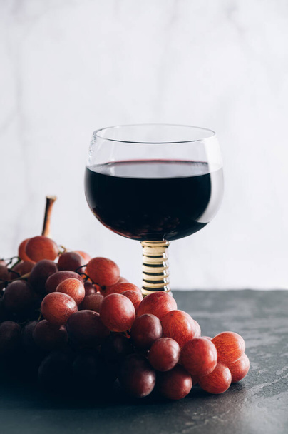 Glass of red wine with red grapes nearby, white background - Фото, зображення