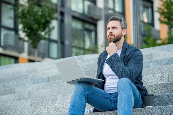 thinking freelancer man with laptop working online. communication online of man freelancer with laptop. concept of freelance. freelancer man work online on laptop outdoor. - Foto, immagini