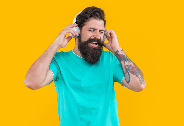 studio shot of cheerful guy with headphones. cool guy listen music. bearded guy listen music in headphones isolated on yellow background. guy listen music in headphones. listen to music concept. - Photo, Image