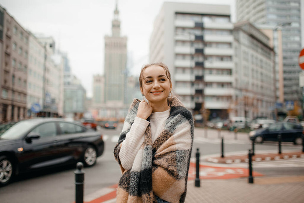 歯で微笑む幸せな若い大人の女性は屋外で笑顔と冬服やニットスカーフを身に着けて街を歩く. - 写真・画像