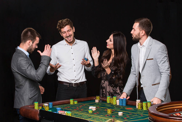 Group of young people behind roulette table on black background. The young man rejoices victory - Photo, Image
