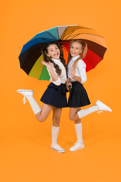 Primary school fashion. Happy school kids with fashion look holding colorful umbrella. Fashion small girls in formal uniforms smiling on yellow background. School fashion for little children. - Фото, изображение