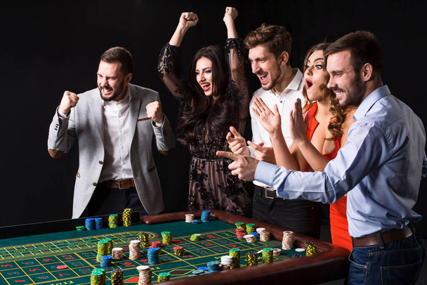 Grupo de jóvenes detrás de la mesa de ruleta sobre fondo negro. Emociones jugadores - Foto, Imagen