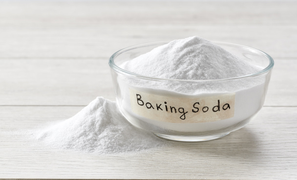 baking soda in a clear glass bowl on a light wooden table. Glass bowl of sodium bicarbonate on a white wooden table. - Photo, Image