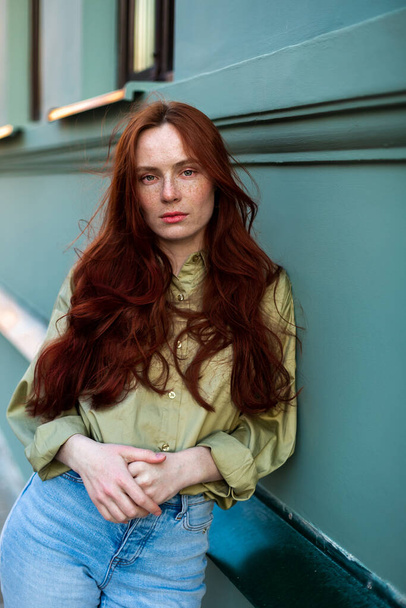 Uzun kızıl saçlı genç bir kadın şehirde poz veriyor. Çilli yüz, yakından, doğal güzellik. Açık havada fotoekonomik durgunluk - Fotoğraf, Görsel