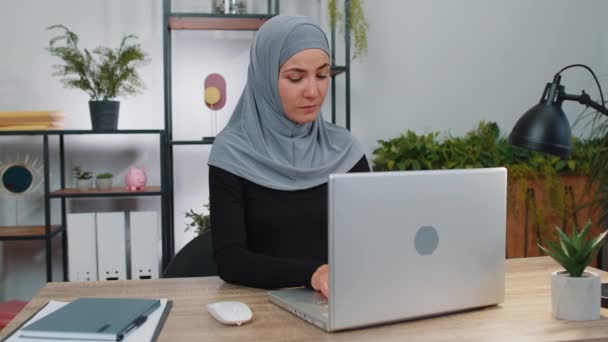 Bizneswoman w hidżabie zamykanie laptopa komputera po zakończeniu pracy w biurze domu. Uśmiechnięty muzułmanin manager freelancer dziewczyna zajęty pracy online, zdalnej pracy. E-learning, przeglądanie Internetu na notebooku - Materiał filmowy, wideo