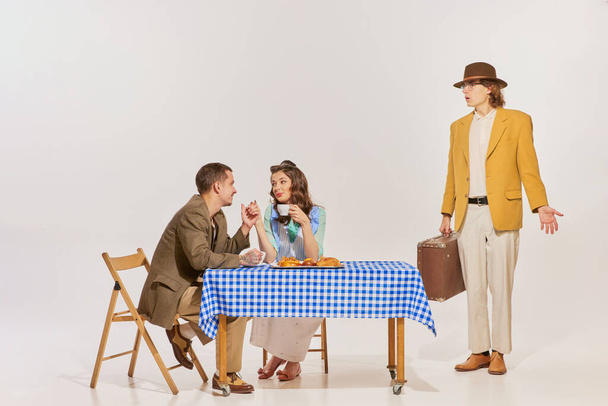 Portret van een mooie jonge vrouw zittend aan tafel met een man over een grijze achtergrond. Echtgenoot keert terug naar huis. Concept van schoonheid, retro stijl, mode, elegantie, jaren 60, 70, familie. Kopieer ruimte voor advertentie - Foto, afbeelding