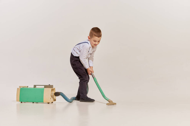 Портрет веселого маленького хлопчика-прибиральника з пилососом ізольовано на сірому фоні. Концепція вінтажного, ретро-стилю, моди, 60-х, 70-х років, сім'ї. Копіювати простір для оголошення
 - Фото, зображення