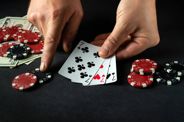 The player bets on a winning combination of three of a kind or a set in a poker game on a black table with chips and money in a club - Photo, Image