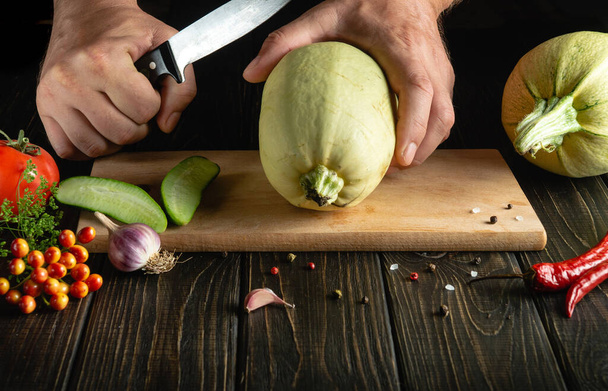 Ahşap bir kesme tahtasının üzerinde aşçının elleriyle pişirmeye hazırlanmadan önce sebze iliğini bıçakla dilimlemek. Aşçılıkta, kabağın kalın eti kullanılır. - Fotoğraf, Görsel