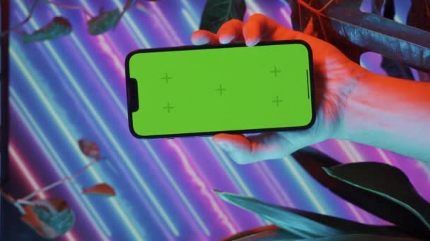 Verticale video van mannelijke hand telefoon met groen scherm tegen neon bloemen. Hoge kwaliteit 4k beeldmateriaal - Video