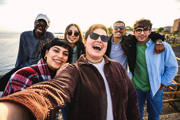 Ryhmä onnellisia monikansallisia ystäviä hetki merenrannalla onnellista monipuolista ystäväryhmää nauttimassa kauniista aurinkoisesta päivästä älypuhelimen muotokuvan ottaminen selfietä auringonlaskun aikaan nuoret käyttävät teknologiaa ja pitävät hauskaa - Valokuva, kuva