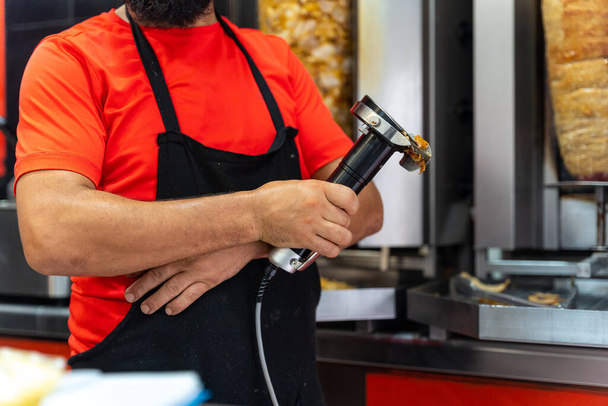 Chef of the kebab restaurant, using the electric tool to cut doner meat from the grill - Photo, Image