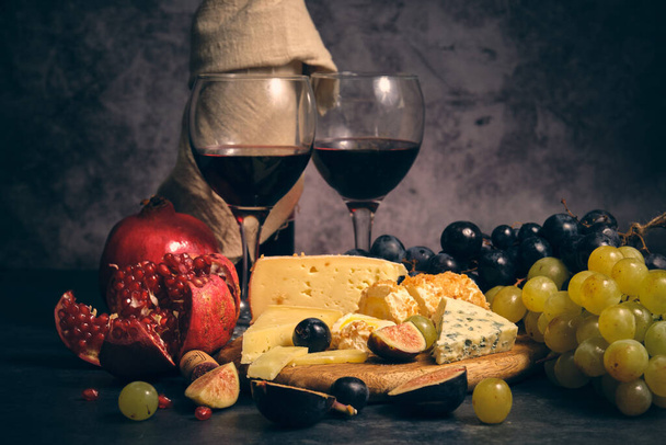 Натюрморт бутылка вина пара бокалов различных сыров и фруктов виноград инжир и гранат - Фото, изображение