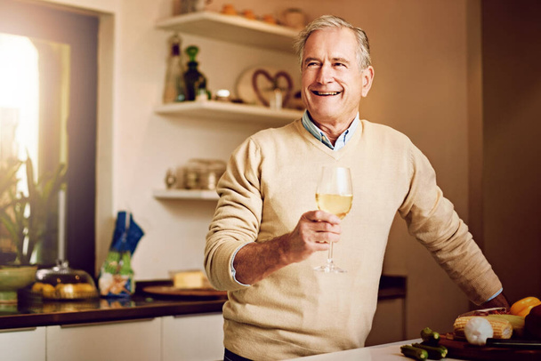 Stejně jako sýr a víno jsem se s věkem zlepšil. starší muž si vychutnává sklenku vína při přípravě večeře ve své kuchyni - Fotografie, Obrázek