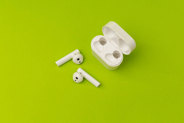 Auriculares inalámbricos en blanco sobre un fondo verde colorido, auriculares publicitarios - Foto, imagen