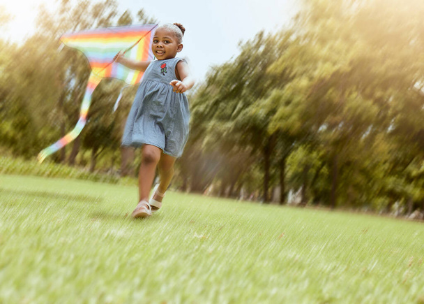 Girl, running with kite and nature park for happy, fun outdoor activity and freedom run in summer making childhood memory. Playful child, grass field and black kid playing outside on nature holiday. - Фото, изображение