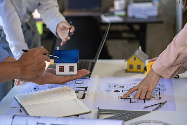 Architects and engineers point to buildings on blueprints and use laptops to draw house project designs in a construction concept office. - Foto, imagen