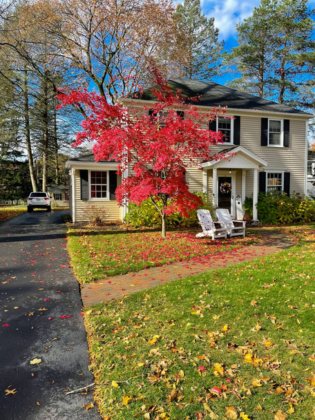 Pitkä ajomatka johtaa kaksi kerroksinen talo värikäs punainen vaahtera lehdet ja valkoinen Adirondack tuolit etukuistilla lähiöissä Rochester, New York, USA. Etupihan istuimet ja asuintilat syksyllä - Valokuva, kuva