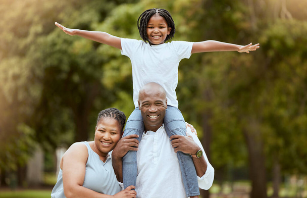 Portrait of a happy black family in nature to relax bonding in freedom, wellness and peace together in a park. Mother, father and child loves flying, hugging or playing outdoors enjoying quality time. - Photo, Image