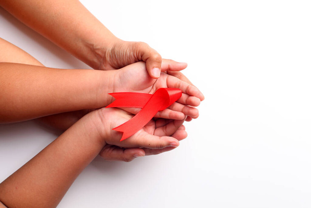Woman's hand and child's hand holding red ribbon together over white with copyspace. Aids day concept - Foto, immagini