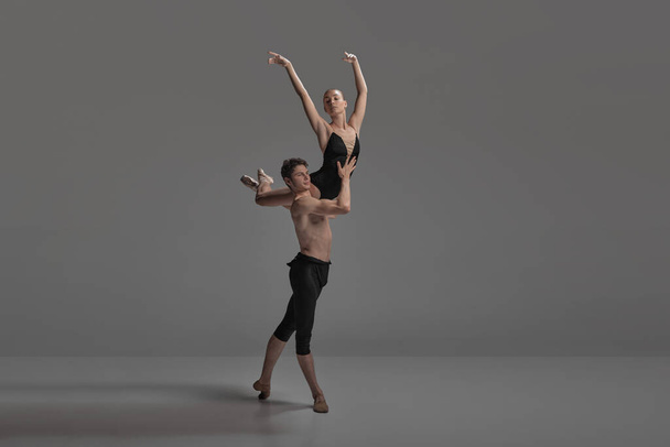 Young man and woman, ballet dancers performing isolated on dark grey studio background. Keeping balance on shoulder. Concept of classical dance aesthetics, choreography, art, beauty. Copy space for ad - Photo, Image