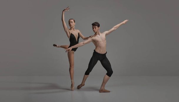 Young man and woman, ballet dancers performing isolated over dark grey studio background. Artistic movements. Concept of classical dance aesthetics, choreography, art, beauty. Copy space for ad - Fotoğraf, Görsel