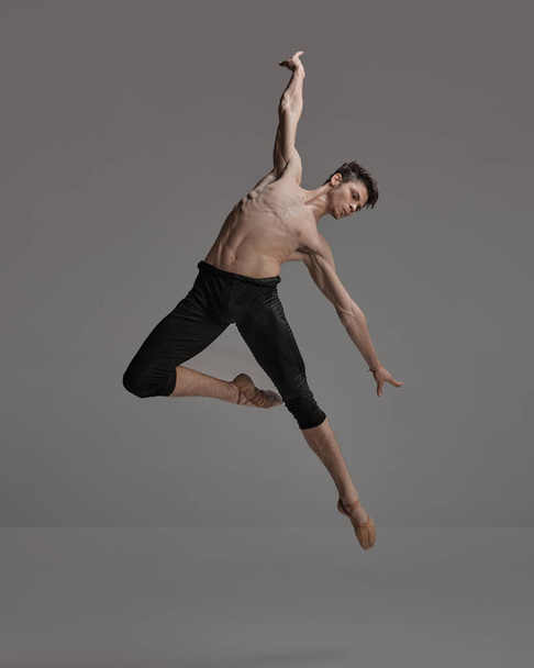 Portrait of young muscular man, ballet dancer performing isolated over dark grey background. Expressing freedom. Concept of classical dance aesthetics, choreography, art, beauty. Copy space for ad - Foto, Imagem