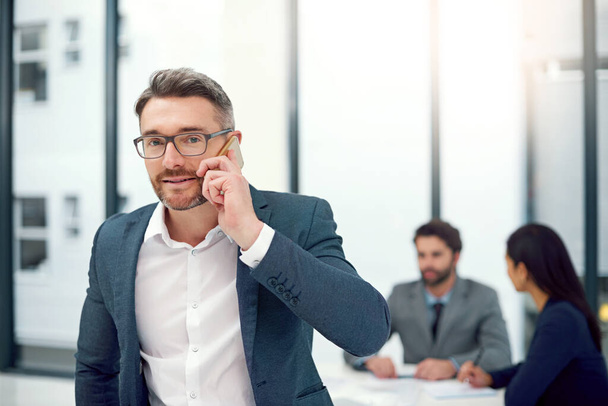 Ein paar professionelle Ratschläge. Porträt eines Geschäftsmannes, der während einer Vorstandssitzung mit Kollegen im Hintergrund telefoniert - Foto, Bild