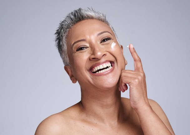 Skincare, cream or happy senior woman, healthy skin or smile for beauty product on face against grey studio background. Elderly latino model happiness, cosmetic wellness and sunscreen for body health. - Photo, Image