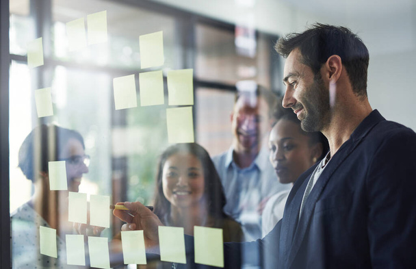 Planejar é um esforço de equipe. um grupo de empresários que trabalham em uma parede de vidro no escritório - Foto, Imagem