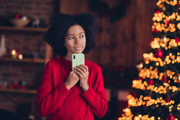 Portrait of minded peaceful small girl hold telephone contemplate idea plan imagine christmastime spirit indoors. - Foto, afbeelding