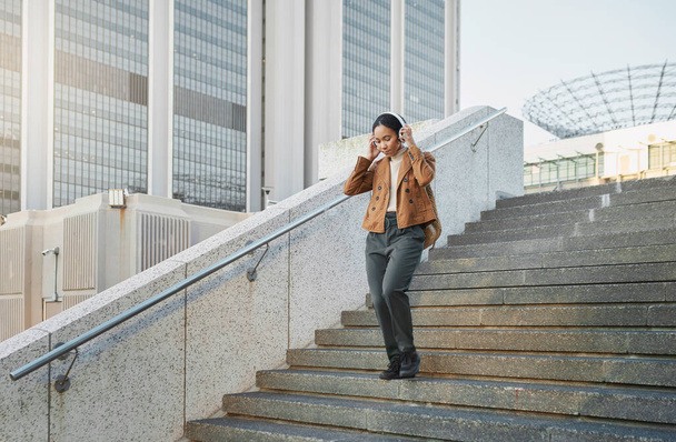 Music, stairs and city with a business black woman walking outdoor while using headphones for streaming audio. Steps, commute and listening with a female employee streaming audio in an urban town. - Photo, Image